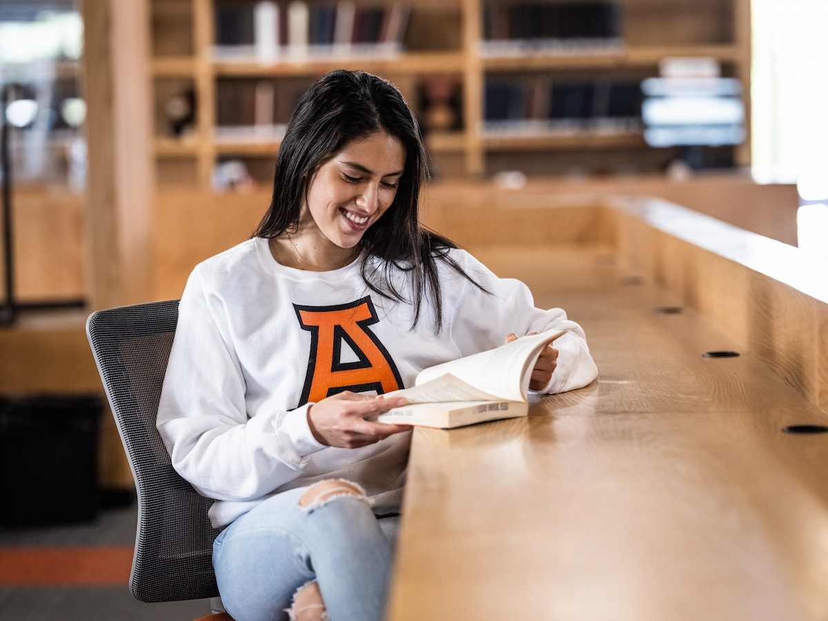 Estudiante de la Licenciatura en Idiomas leyendo con interés en una biblioteca, reflejando estudio autónomo, pasión por las lenguas y ambiente académico.