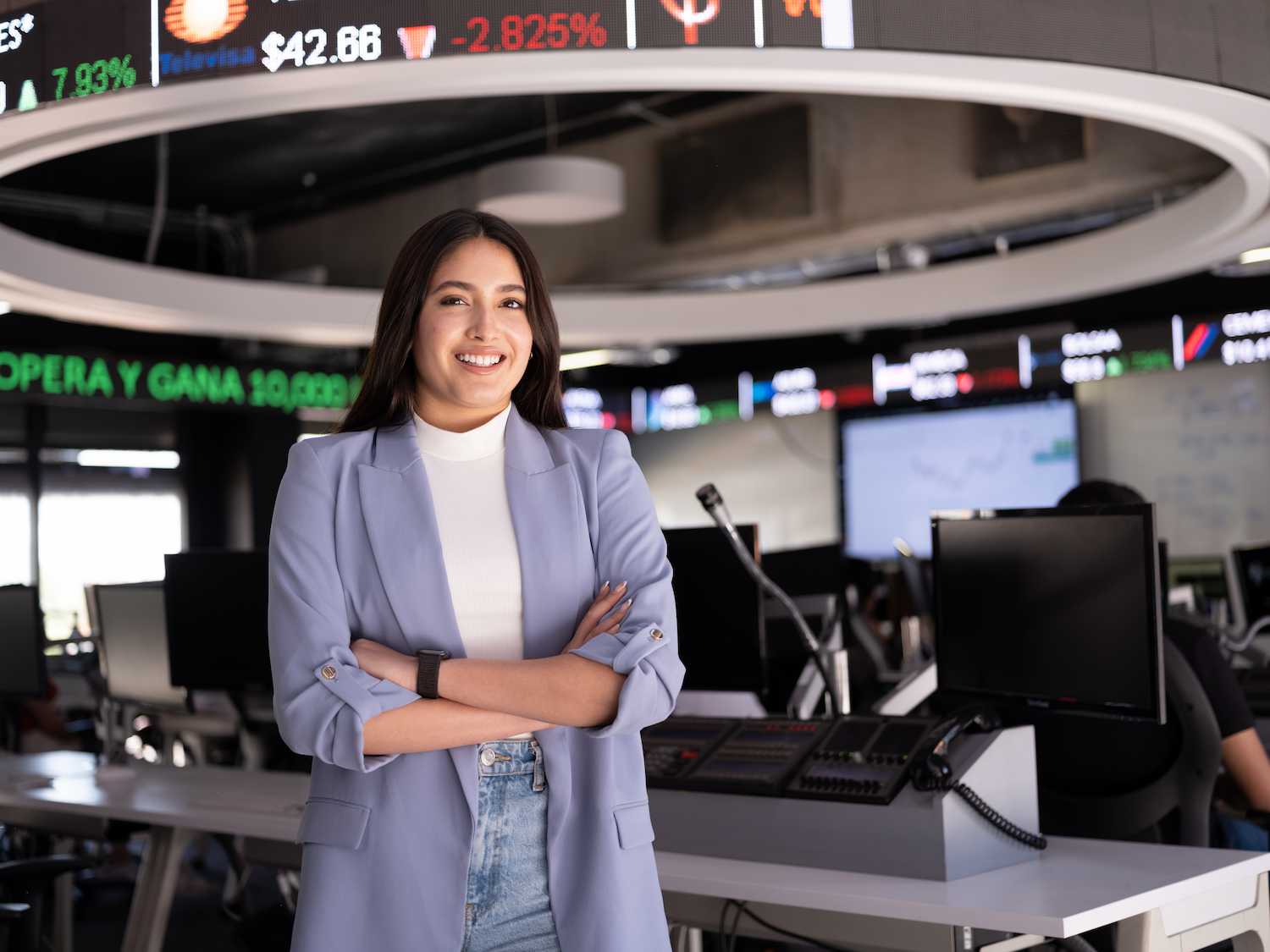 Estudiante universitaria posando con confianza frente a pantallas de información financiera en un aula moderna de la Universidad Anáhuac.
