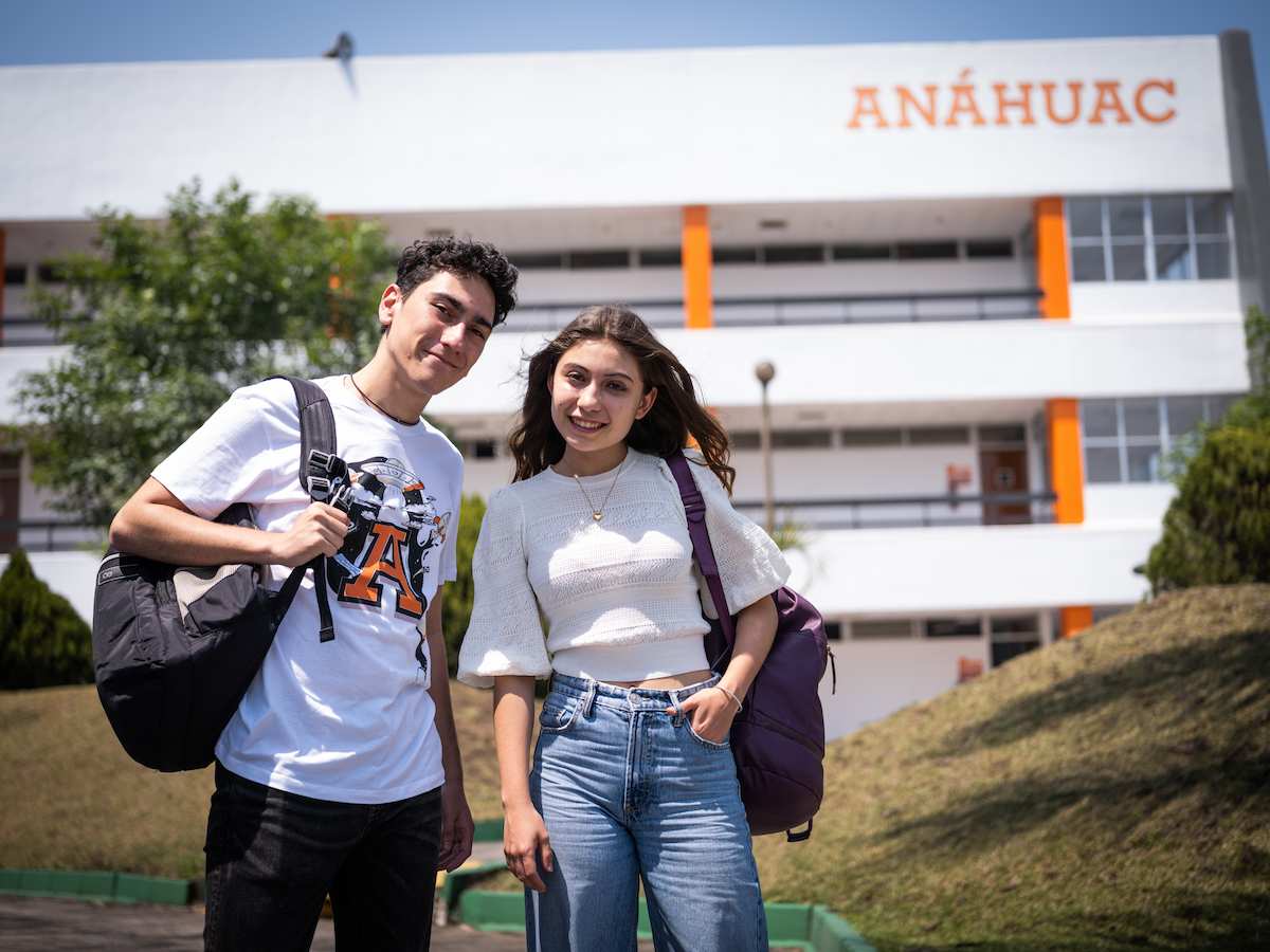 Pareja de estudiantes frente al edificio de la Universidad Anáhuac, mostrando una actitud positiva y conectando con el espíritu universitario.